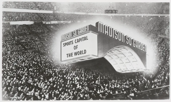 Crowded Madison Square Garden arena with a large illuminated sign proclaiming it the 'Sports Capital of the World.'