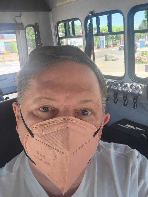 Man wearing a KN95 mask. Pupils dilated after doctor visit. Seated inside a van with windows. 