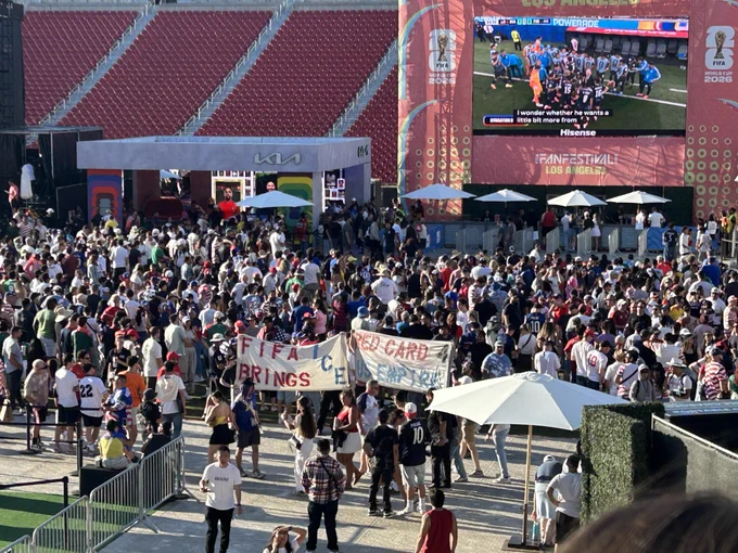 A crowd of soccer fans with 4 people holding 2 banners in the middle, the banners read FIFA BRINGS ICE and RED CARD 4 US EMPIRE