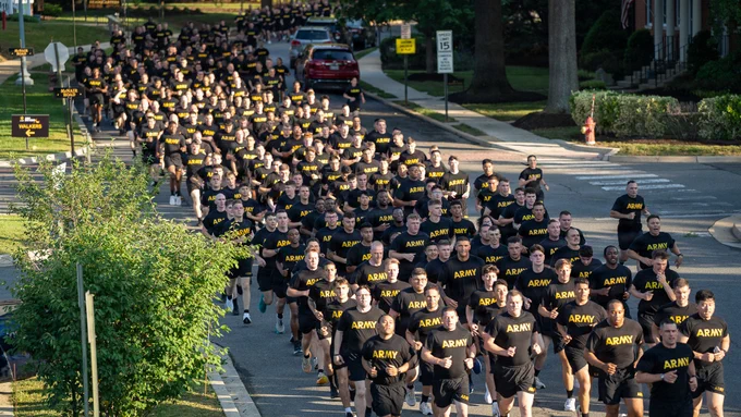 A high-angle view showing hundreds of U.S. Army Soldiers running in a tight formation down a residential street during the Army's 251st Birthday Run at Joint Base Myer-Henderson Hall, Virginia, June 12, 2026. The Soldiers are wearing matching black physical training t-shirts with \"ARMY\" printed in yellow.