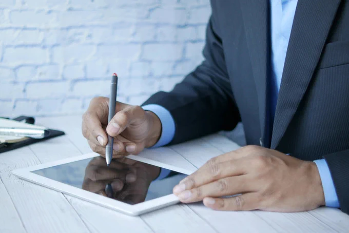 A close up of a person working in a suit and writing on an ipad.