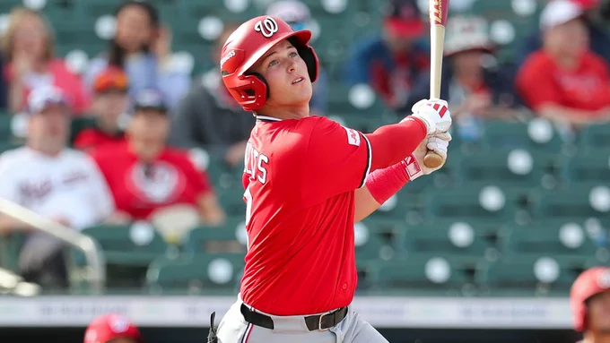 Eli Willits follows through on his swing wearing a red Washington Nationals jersey, helmet and gray pants