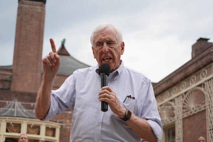 Congressman Steny Hoyer delivers a speech in front of a brick building. He appears to be outdoors.