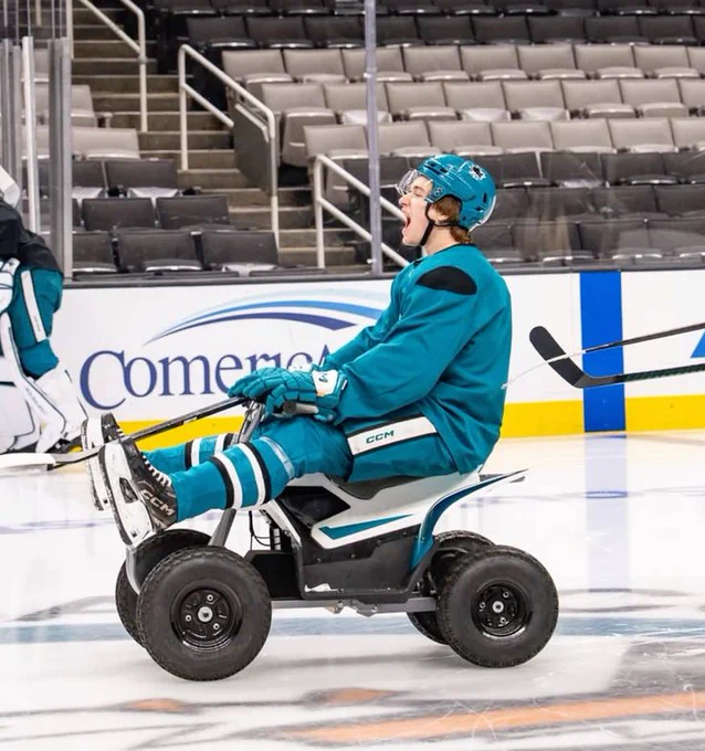 Macklin Celebrini on the ice in a teal practice outfit driving Sharkie's ATV