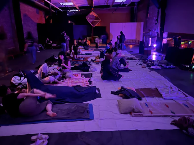 Photo in a purple light room, with a bunch of people getting ready to sleep.