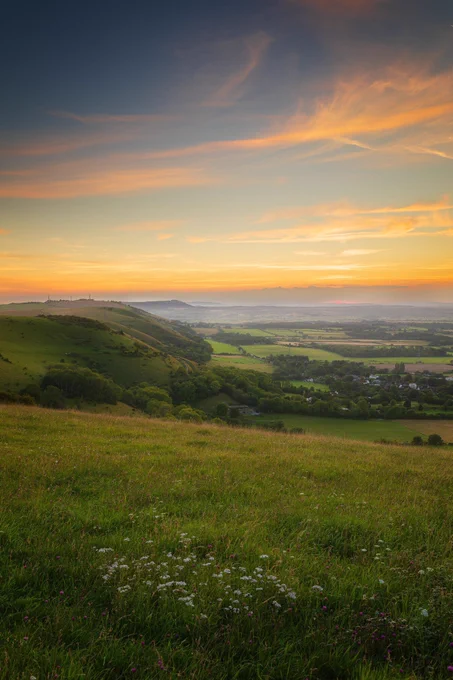 Blue‑orange sunset sky over a lush green landscape with soft mist drifting in the distance.