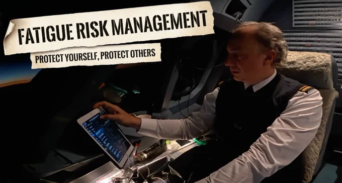 A pilot in white uniform shirt with gold epaulettes in a dim night cockpit, leaning to work on a tablet, the low dawn light on the horizon through the windscreen — visibly tired. Two torn-paper magazine-cutout ribbons in bold black stencil capitals overlay the photo: a top ribbon reading 'FATIGUE RISK MANAGEMENT' and a lower ribbon reading 'PROTECT YOURSELF, PROTECT OTHERS.'