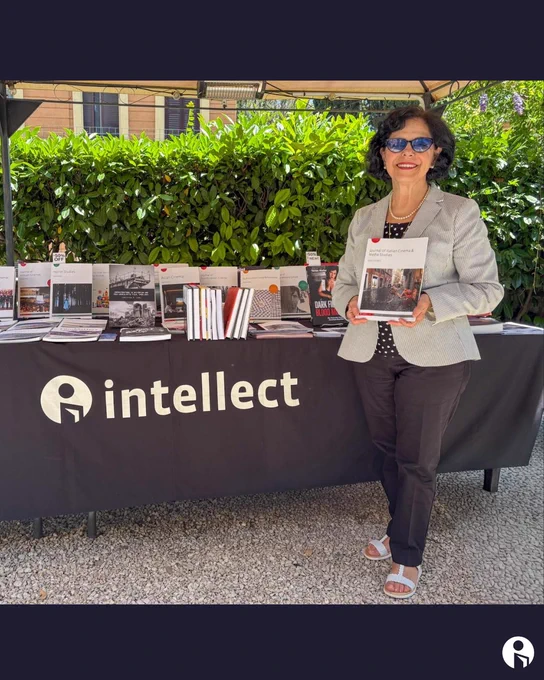 Person standing beside a table covered with a black cloth displaying the 'intellect' logo and various books arranged on top outdoors.
