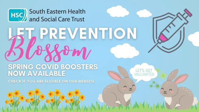 The image is a promotional graphic from the South Eastern Health and Social Care Trust. It features a spring theme with two cartoon rabbits surrounded by flowers and grass. One rabbit has a speech bubble saying, "Let's get vaccinated." A message reads, "Let prevention blossom. Spring COVID boosters now available. Check if you are eligible on our website." A large syringe illustration is shown in the sky.