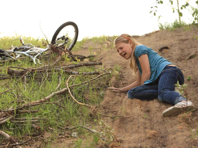 Noia al terra en una caiguda amb una bicicleta en un camí rural.