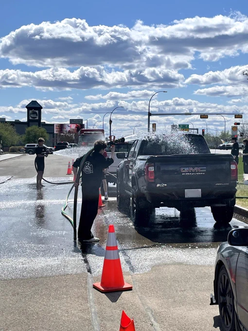 Fire Cadets wash a black pickup truck on a sunny day.