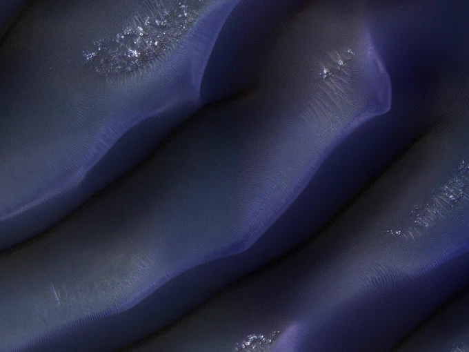 Enhanced color closeup of an aerial view of large dunes on the surface of Mars. There is flat terrain between the three sections of dunes in this image.