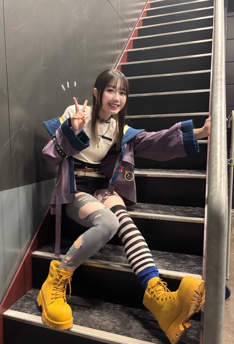 須賀蕾叶モジュールの橘めいの他撮り写真です。
全身写っていて、階段に座っております。
右手でピース、左手は階段に取り付けられた手すりの支えを掴んでいます。
右足を軽く折り曲げ左足を伸ばして座っています。

カメラ目線で笑顔です。