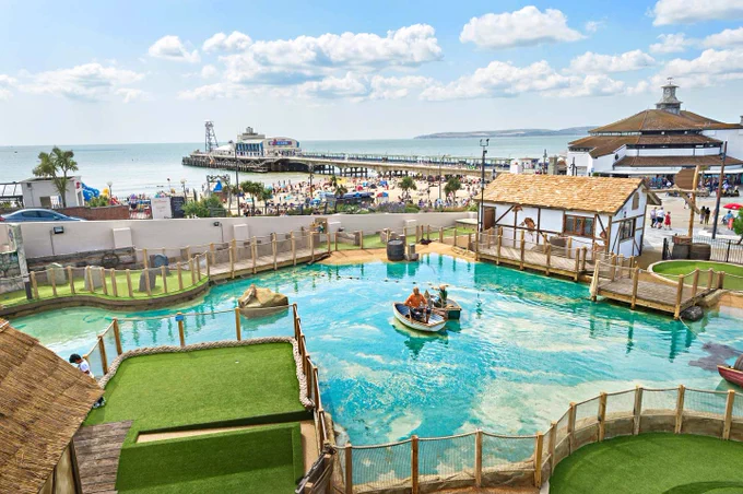 A view of Bournemouth's outdoor swimming pool in the foreground, with Bournemouth Pier extending into the sea and the coastline visible in the background.