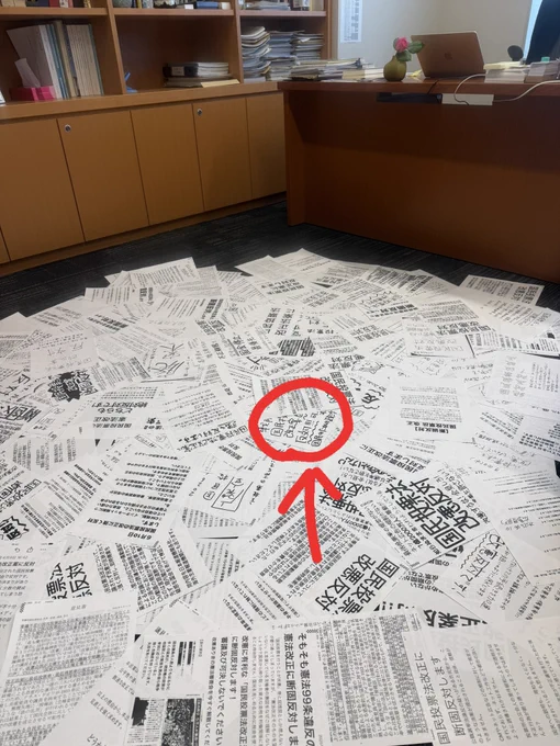 床に広げられたFAXの紙の中で1枚に赤い丸をつけている写真