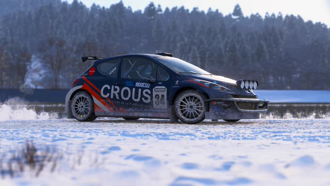 A rally car with "Crous" on the side is driving on a snowy track. The surrounding area features snow-covered trees under a clear sky.