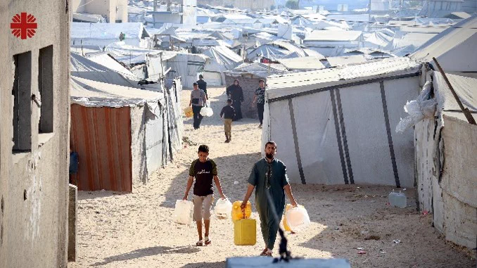 A man and boy walking through tents carrying water containers.