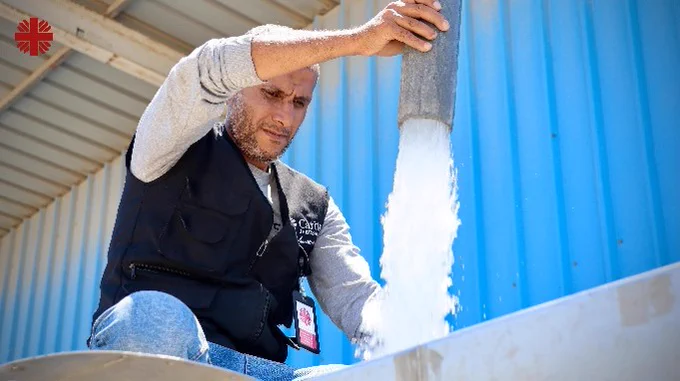 A Caritas aid worker using a hose as it pours fresh water. 