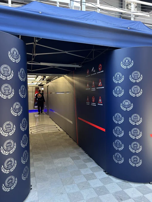 Entrance to the Oracle Red Bull Racing garage at the Spanish Grand Prix, flanked by navy panels displaying the team’s Drivers’ and Constructors’ Championship laurels from 2010 through 2024. Safety signage covers the wall, and a team member in Red Bull kit walks down the polished garage corridor.