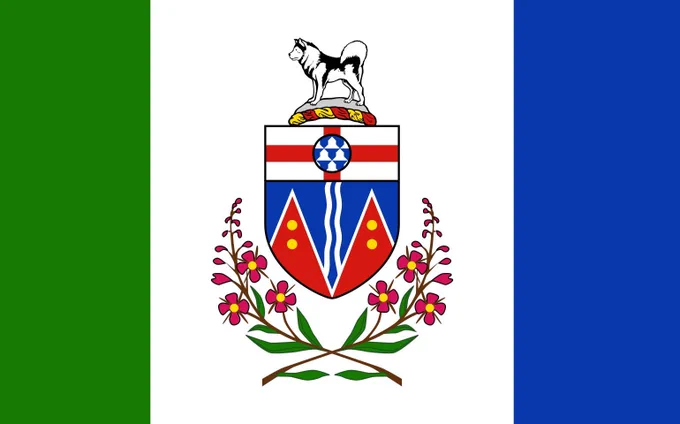 Yukon flag with three vertical bands of green, white, and blue. In the centre white band is a coat of arms with a shield, red and blue sections, white wavy lines, gold circles, and a husky standing above it. Pink fireweed flowers with green leaves curve below the shield.
