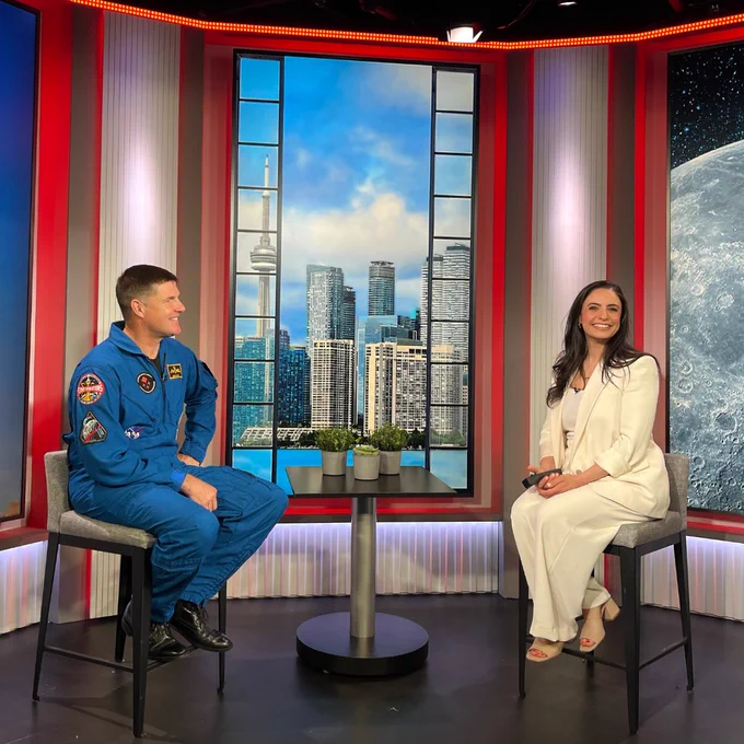 L'astronaute Jeremy Hansen lors d'une entrevue télévisée en studio avec la ligne d'horizon de Toronto en arrière-plan.