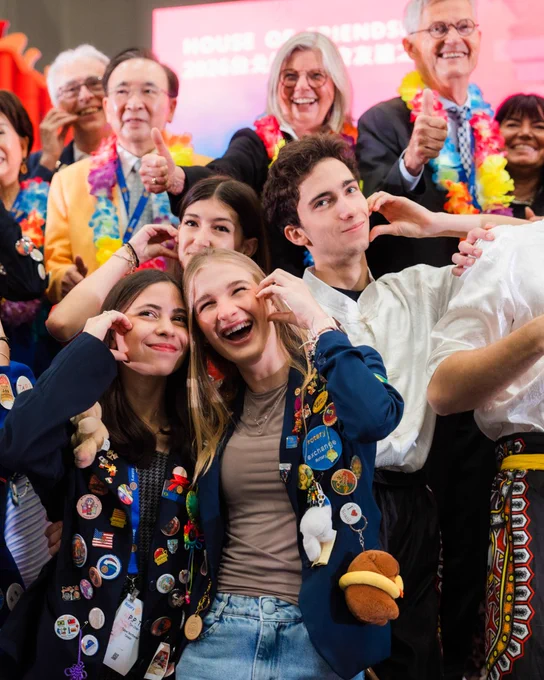 A group of people smiling and posing for a photo, some wearing colorful leis and others displaying jackets adorned with various pins and patches.