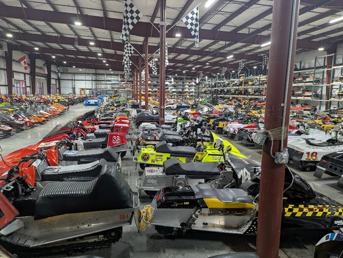 A large number of unidentified snowmobiles located inside a warehouse. 