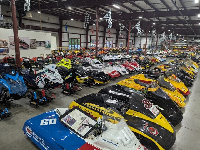 A large number of unidentified snowmobiles located inside a warehouse. 