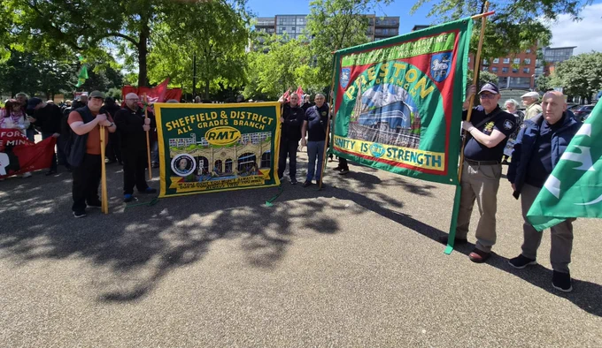 Group of people holding colorful union banners for Sheffield & District and Preston on a sunny day in a park.