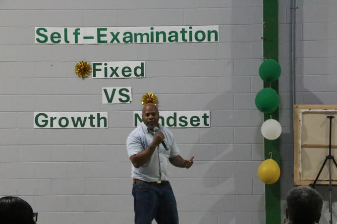 Man speaking in front of a wall with the words 'Self-Examination Fixed VS Growth Mindset' displayed in green letters.