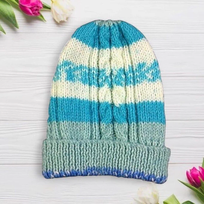 Chunky knit beanie in mint, turquoise and cream stripes on white wood. Tulips frame corners. Bright light shows texture and colour clearly.