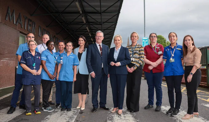 Image of 13 people standing in a row - First Minister Michelle O’Neill, deputy First Minister Emma Little-Pengelly, and Health Minister Mike Nesbitt with staff from the Mater Hospital.