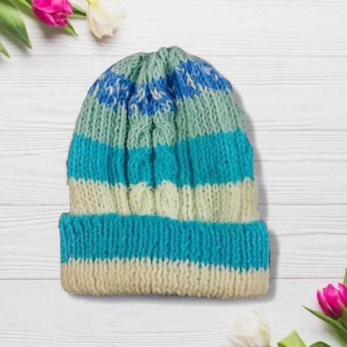 Chunky knit beanie in mint, turquoise and cream stripes on white wood. Tulips frame corners. Bright light shows texture and color clearly.