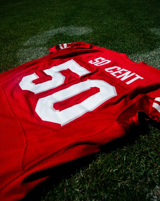 A red football jersey with the name '50 Cent' and number '50' lies on a green grass field. The bright colors and casual placement suggest a sporty and laid-back atmosphere.