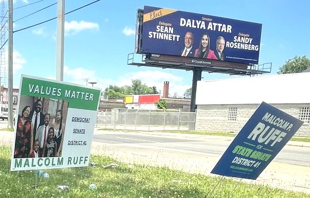 A Dalya Attar billboard looms over Reisterstown Road and the smaller signs positioned by her opponent, Malcolm Ruff, at ground level in front of a gas station. (Fern Shen)