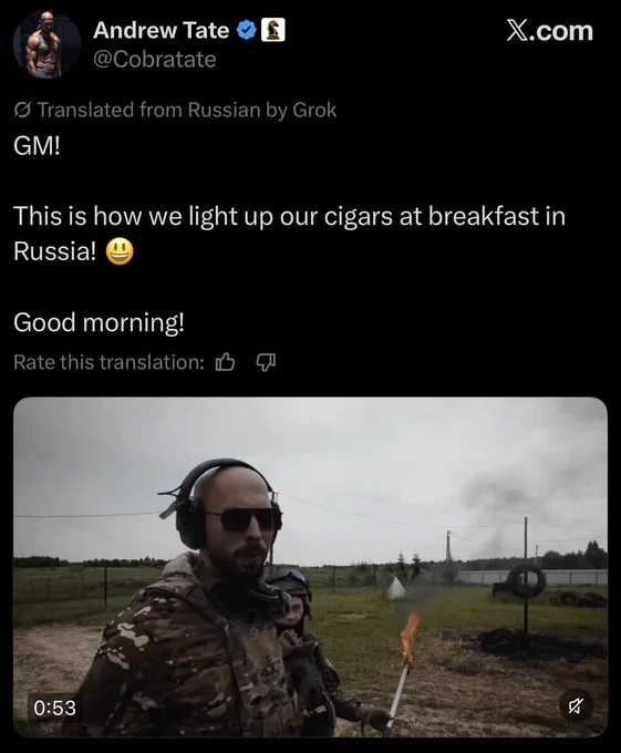 Screenshot of a post from the verified account Andrew Tate, @Cobratate, labeled translated from Russian by Grok. Text reads: GM. This is how we light up our cigars at breakfast in Russia, with a smiling emoji. Good morning. Below is a video thumbnail showing Tate in camouflage gear, sunglasses, and ear protection standing in a field at an outdoor firing range, holding a long lit torch with a flame at the end. A second person in camouflage and a helmet stands behind him. Tires and targets are visible in the background.