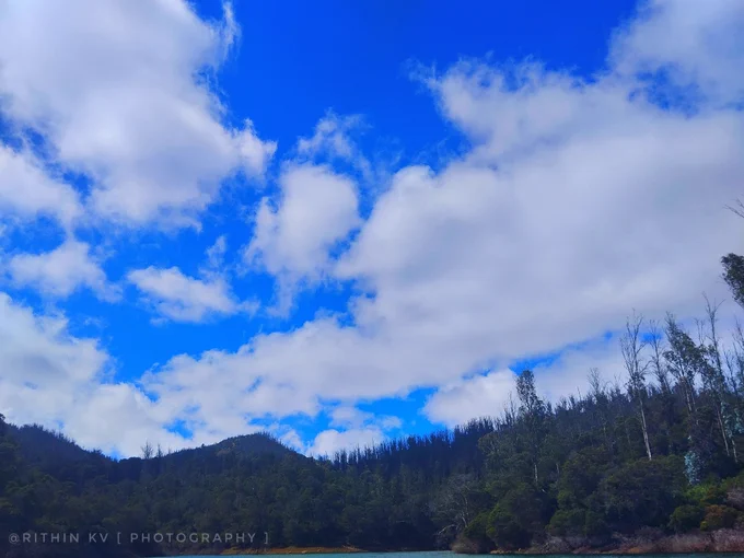 Beautiful landscape showing a bright blue sky filled with white clouds over lush green hills.