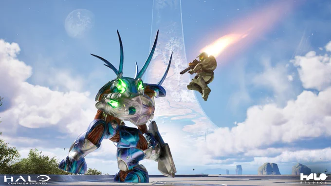 A Hunter standing on a platform, while Master Chief leaps into the air, firing a rocket launcher towards it. The Halo appears in the background with a cloudy sky.