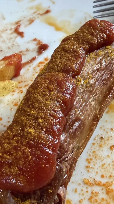 Eine Bratwurst mit Tomatenketchup und Currypulver oben drauf.