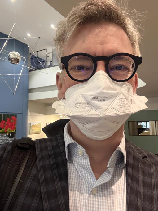 Dr. David Keegan, newly appointed chair of Public Health Agency of Canada’s National Advisory Committee on Preventive Health Services, wearing a 3M V-flex N95 respirator, a plaid jacket and a check shirt, inside a building of The BC Health Ministry.