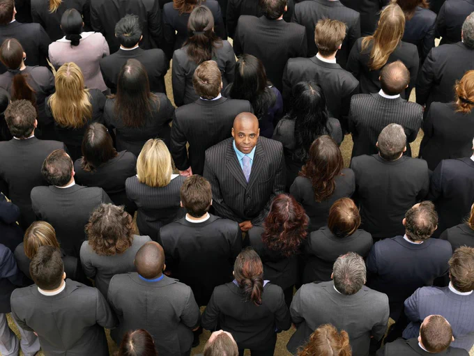 A crowd of people with their backs to the camera, in the middle is one person facing the camera.