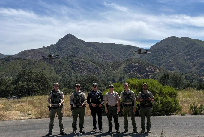 California State Parks rangers peace officers posing in Malibu Creek State Park with two drones overhead.