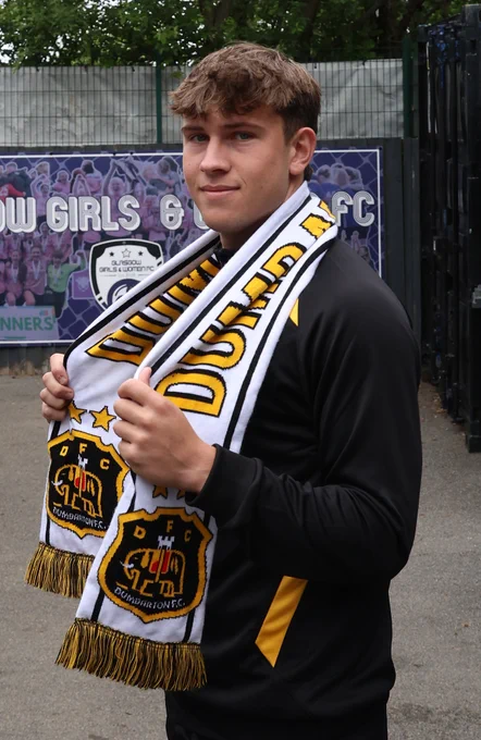 A young man poses outdoors with a Dumbarton F.C. scarf, exuding a sense of pride and connection to the club. The setting is casual with a hint of sports enthusiasm.