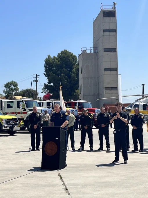 Chief Brian Marshall speaks behind a podium with fire chiefs and firefighting assets behind him.