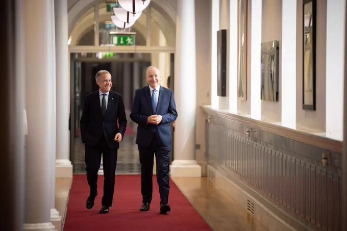 Prime Minister Mark Carney and the Taoiseach of Ireland, Micheál Martin, are walking down a hallway in discussion and smiling.