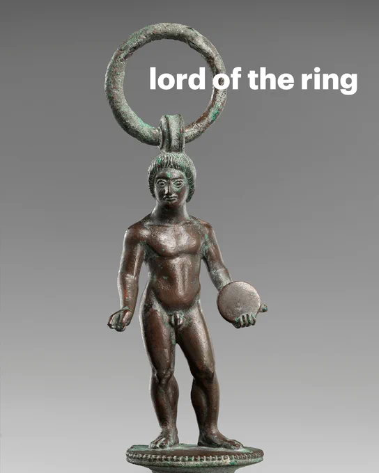 Ancient figurine holding a discus and wearing a large ring on his head. Text: lord of the ring
