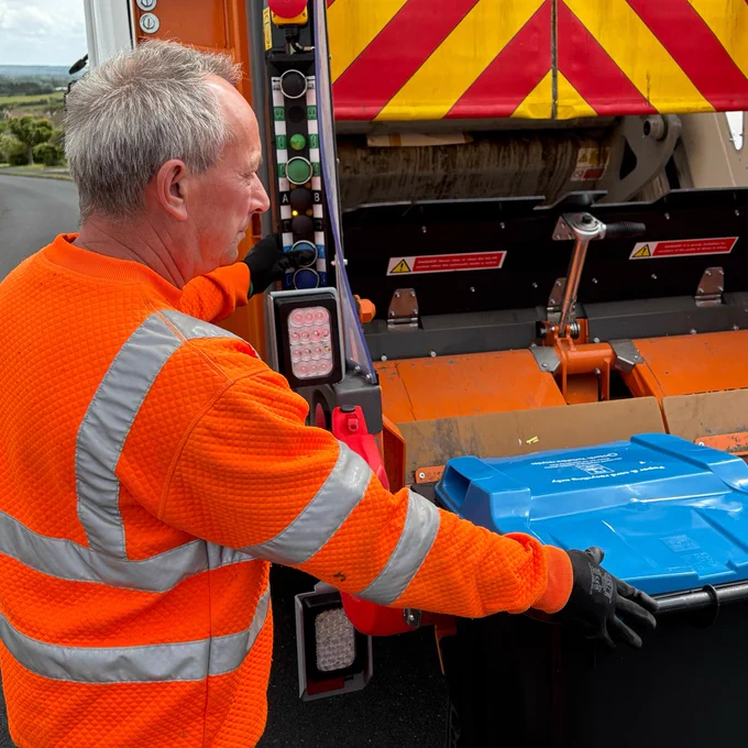 A bin man putting a bin on the back of a lorry