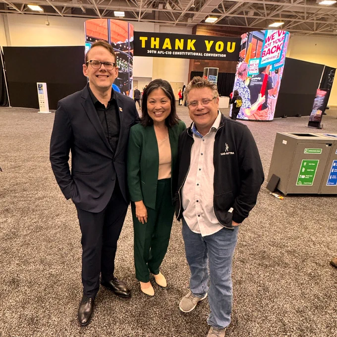 Three people standing together in a large convention hall with a 'THANK YOU' sign in the background at the 30th AFL-CIO Constitutional Convention.
