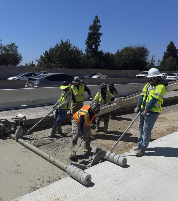 Workers pouring and leveling lean concrete base. 