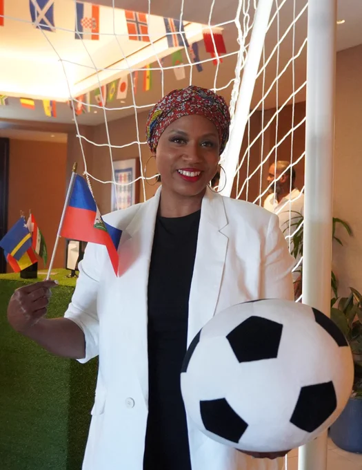 Rep. Ayanna Pressley poses for a photo holding a soccer ball and waving a small Haitian flag.